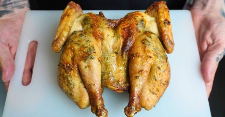 Spatchcock chicken aka buttefly cut chicken cooked and resting on a white cutting board held by two hands